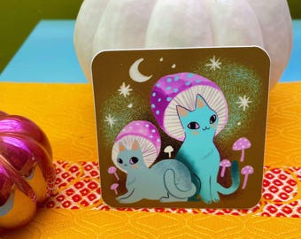 Op de afbeelding: Een vierkante sticker met twee cartoonkatten met paddenstoelenkappen. Eén kat is blauw, de andere is grijs. De achtergrond is bruin met een halve maan en sterren. Er zijn ook kleine roze paddenstoelen aanwezig.