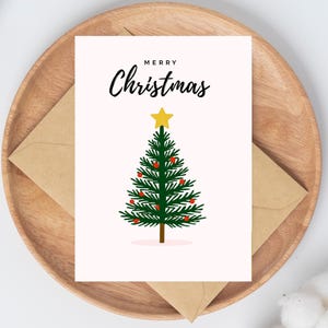 May include: A Christmas card featuring a green Christmas tree with red baubles and a yellow star. The card has the words "MERRY Christmas" in black script. It sits on a wooden tray with a brown envelope.
