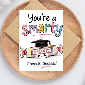 Op de afbeelding: Een afstudeerwenskaart met de tekst "You're a Smarty" in kleurrijke letters. De kaart toont een cartoon Smarty snoepje met een afstudeerhoed. De tekst "Congrats, Graduate!" is ook inbegrepen.
