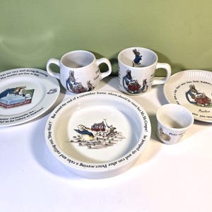 Puede incluir: Un conjunto de vajilla de cerámica blanca de Peter Rabbit que incluye dos platos, dos tazas y un vaso pequeño. Cada pieza presenta ilustraciones coloridas de Peter Rabbit y texto impreso extraído de los cuentos de Beatrix Potter.