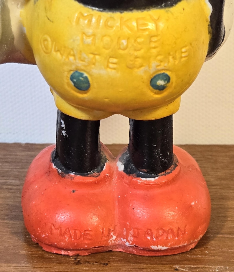May include: A vintage Mickey Mouse figurine, featuring a yellow torso, black legs, and red shoes. The text "MICKEY MOUSE &copy; WALT E. DISNEY" is visible on the torso. The figurine is marked "MADE IN JAPAN" on the bottom.