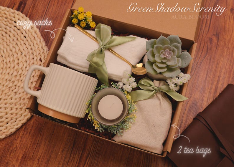 Może przedstawiać: Pudełko prezentowe "Green Shadow Serenity" zawiera biały kubek, przytulne skarpetki, sukulenta, świecę i dwie torebki herbaty. Pudełko jest zawiązane zieloną wstążką i zawiera złoty łyżeczkę. Og&oacute;lna kolorystyka jest neutralna z zielonymi akcentami.