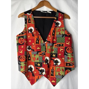 May include: A Halloween-themed vest with a patchwork design. The vest features a black lining and a colorful pattern of pumpkins, cats, moons, stars, and leaves on a red, orange, and green background. It has a button-up front and a V-neck.