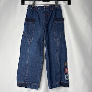 May include: Dark blue denim trousers with navy blue detailing and red stitching. Includes two front pockets and decorative patches with a tree, maple leaf, and cross. Elasticated waistband for comfort.