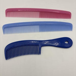 May include: Three plastic hair combs in pink, blue, and navy blue. The pink and blue combs are rectangular, while the navy blue comb has a handle with a hole. The blue comb has the word "Unbreakable" printed on it.