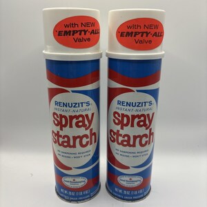 May include: Two cans of Renuzit's Instant-Natural spray starch. The cans are cylindrical with a white top and a blue and red striped design. The label reads "spray starch" in large red letters. Each can has a red sticker that says "with NEW EMPTY-ALL Valve".