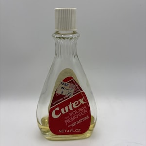 May include: A clear glass bottle of Cutex Oily Polish Remover with a white cap. The bottle has a red and white label with the brand name and product information. The bottle contains a yellow liquid and is labeled as 118 ml.