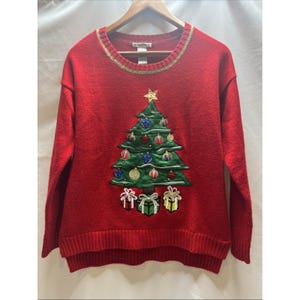 May include: A red Christmas jumper with a crew neck and long sleeves. The jumper features an embroidered Christmas tree decorated with baubles and topped with a gold star. Three gift boxes are embroidered below the tree.