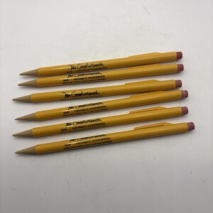 May include: Six yellow mechanical pencils with pink erasers and tan tips. Each pencil features the black text Mr. Goodwrench, NEW - PAPERMATE SHARPWRITER, and PRICE INCLUDES: LOGO & DEALER IMPRINT printed along the barrel. The pencils have a pocket clip.