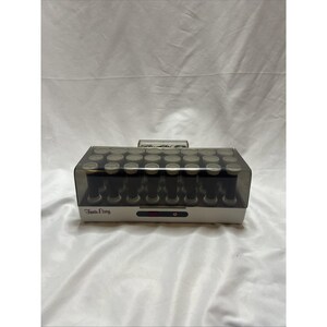 Puede incluir: Un juego de rizadores de pelo blanco y gris con una tapa de plástico transparente. El juego de rizadores tiene un asa en la parte superior y las palabras "Twin Easy" impresas en la parte delantera.