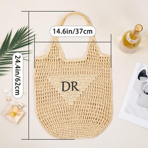 May include: A beige woven tote bag with a heart-shaped design and the initials "DR". The bag is 14.6 inches wide and 24.4 inches tall. The image also includes a bottle of champagne, sunglasses, and perfume.