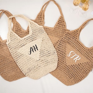 May include: Three woven tote bags in shades of tan and cream. One bag features the initials "AH" in black, and another has "STR" in white. The bags have long handles and a netted design, perfect for beach or market.