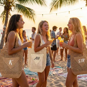 May include: Three women on a beach at sunset, each holding a cocktail and a personalized tote bag. The bags are woven with a heart design and initials. Palm trees and string lights are in the background.