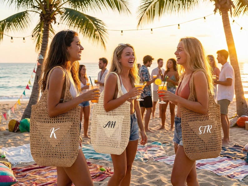 May include: Three women on a beach at sunset, each holding a cocktail and a personalized tote bag. The bags are woven with a heart design and initials. Palm trees and string lights are in the background.