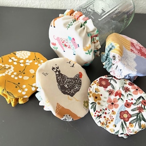 May include: A collection of six fabric bowl covers in various patterns and colors. Designs include floral, animal, and geometric prints. The covers are gathered at the edges and appear to be reusable.