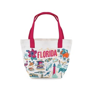 May include: White tote bag with red handles featuring a colorful Florida-themed design. The design includes the word "Florida" in red, along with illustrations of a hibiscus flower, orange, lighthouse, and other Florida icons.