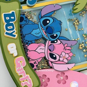 May include: A layered paper craft featuring the characters Stitch and Angel from Lilo & Stitch. The design includes a blue and pink color scheme, with the words "Boy or Girl" on a green banner. The background has gold confetti.