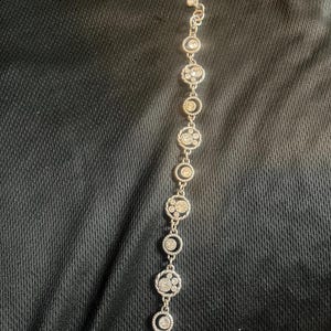 May include: Silver bracelet with a series of circular links. Each link is decorated with clear, sparkling crystals, creating a delicate design. The bracelet has a lobster clasp closure.