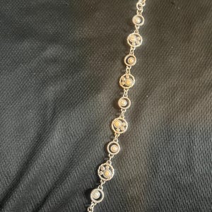 May include: Silver bracelet with circular links, each containing a central beige stone and smaller stones within a decorative silver border. The bracelet fastens with a lobster clasp. The design is symmetrical.