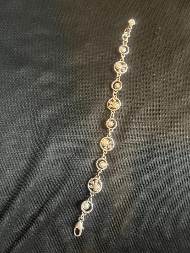 May include: Silver bracelet with circular links, each containing a central beige stone and smaller stones within a decorative silver border. The bracelet fastens with a lobster clasp. The design is symmetrical.