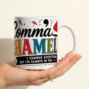 以下が含まれることがあります： さまざまな色で「Comma Chameleon」というテキストが書かれた白いセラミックマグ。マグには「I change everything but I'm always in the right」というテキストもあります。マグは手で持たれています。