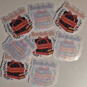 Könnte beinhalten: Sieben bunte Aufkleber mit dem Wort "Bookoholic" und einem Stapel Bücher mit einer Schleife oben drauf. Die Aufkleber befinden sich auf einem weißen Hintergrund.