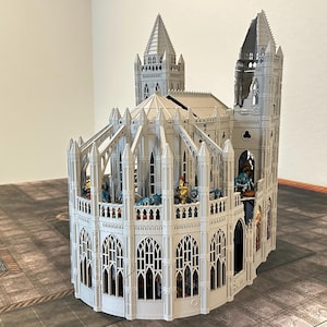 May include: A detailed, white miniature cathedral model with multiple spires, arched windows, and intricate architectural details. The model is partially assembled and sits on a patterned surface, suggesting a tabletop game setting.
