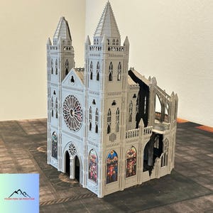 May include: A detailed, gray 3D-printed model of a cathedral with intricate architectural details, including spires, arched windows, and a rose window. The model features stained glass windows and is set on a textured surface.