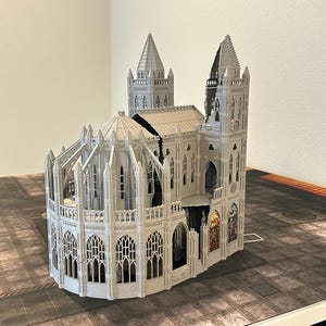 May include: A detailed, gray miniature cathedral model with intricate architectural details, including spires, arched windows, and decorative elements. The model is set on a textured surface, suggesting a tabletop game setting.
