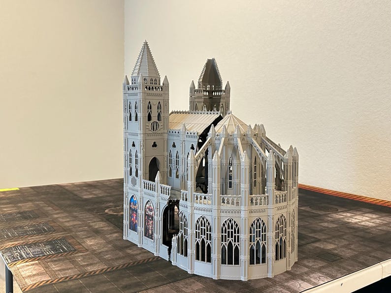 May include: A detailed, light gray model of a cathedral with multiple spires, arched windows, and intricate architectural details. The model is set on a textured surface, showcasing its gothic design.