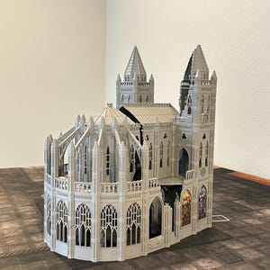 May include: A gray miniature cathedral model with detailed architectural features, including arched windows, spires, and a domed roof. The model has a gothic design and is placed on a patterned surface.