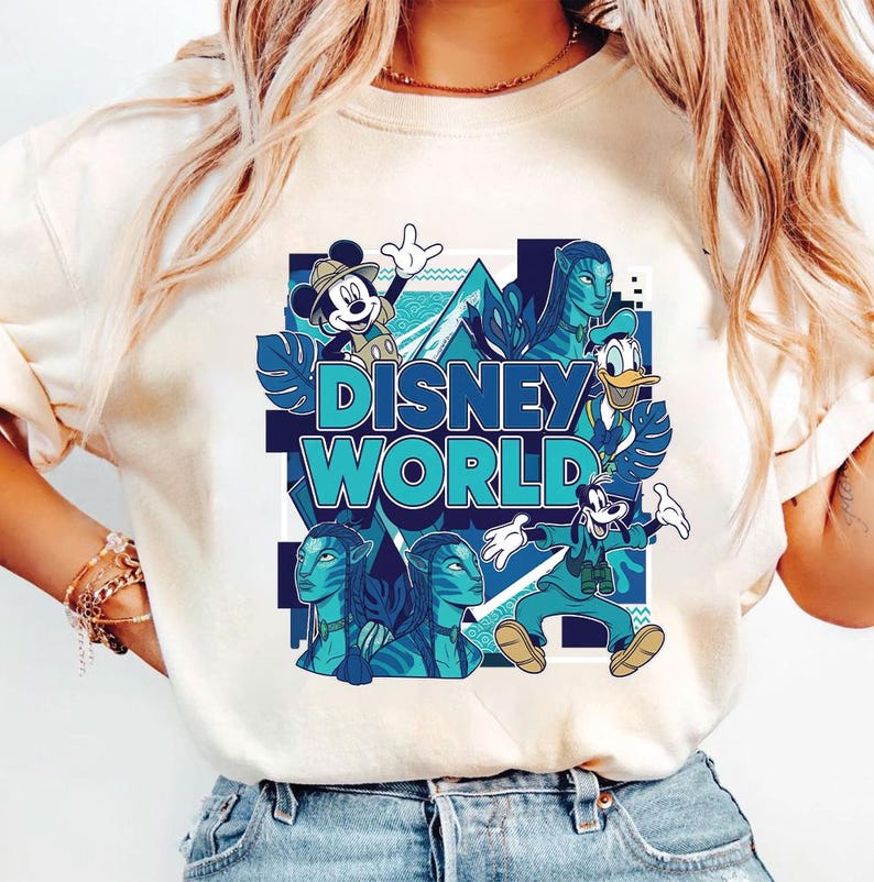 Puede incluir: Camiseta color crema con un vibrante gr&aacute;fico de Disney World. El dise&ntilde;o incluye a Mickey Mouse, el Pato Donald y personajes de Avatar, todos en tonos azules y turquesas. Las palabras "Disney World" se muestran de forma destacada.