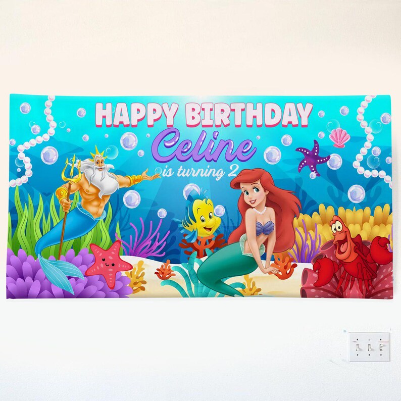 May include: A rectangular banner featuring an underwater scene with the text HAPPY BIRTHDAY Celine is turning 2. The design includes illustrations of a mermaid, a merman with a trident, a yellow fish, and a red crab, surrounded by bubbles and coral.