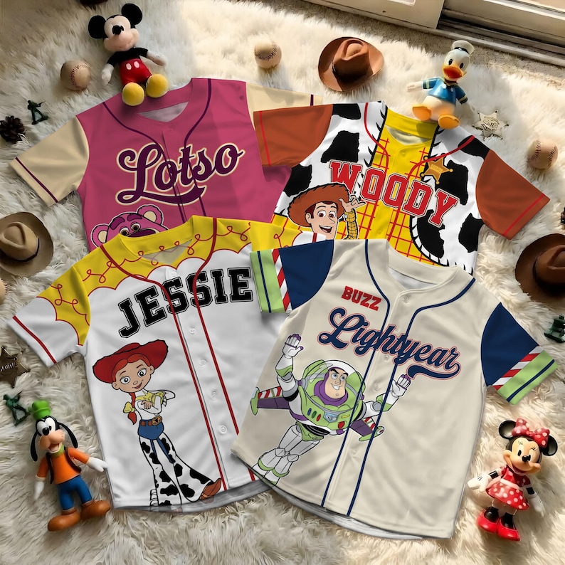 May include: Baseball-style jerseys featuring characters from the animated film Toy Story. The jerseys are pink, yellow, and cream-colored, with character names and images. The jerseys include Lotso, Woody, Jessie, and Buzz Lightyear. The jerseys are displayed on a fluffy white surface.