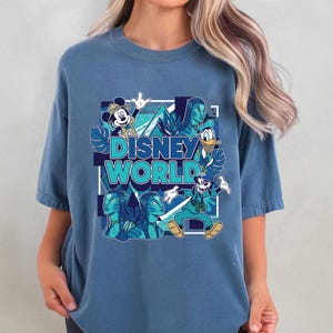 Puede incluir: Una camiseta azul con un dise&ntilde;o de Disney World. El dise&ntilde;o incluye a Mickey Mouse, el Pato Donald, Goofy y personajes de Avatar, con las palabras "Disney World" en turquesa.