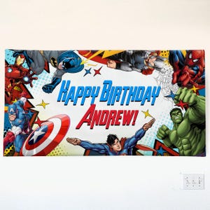 May include: A rectangular banner featuring various comic book superheroes including Iron Man, Batman, Thor, Spider-Man, Captain America, Hulk, and Superman. The text "Happy Birthday Andrew!" is printed in the center in blue and red lettering.