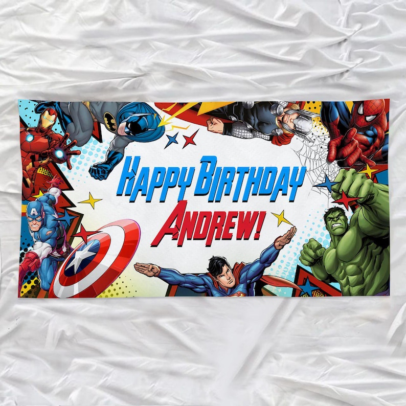 May include: A rectangular birthday banner featuring comic book illustrations of Iron Man, Batman, Thor, Spider-Man, Captain America, Superman, and the Hulk. The text reads Happy Birthday Andrew! in blue and red lettering against a white background.