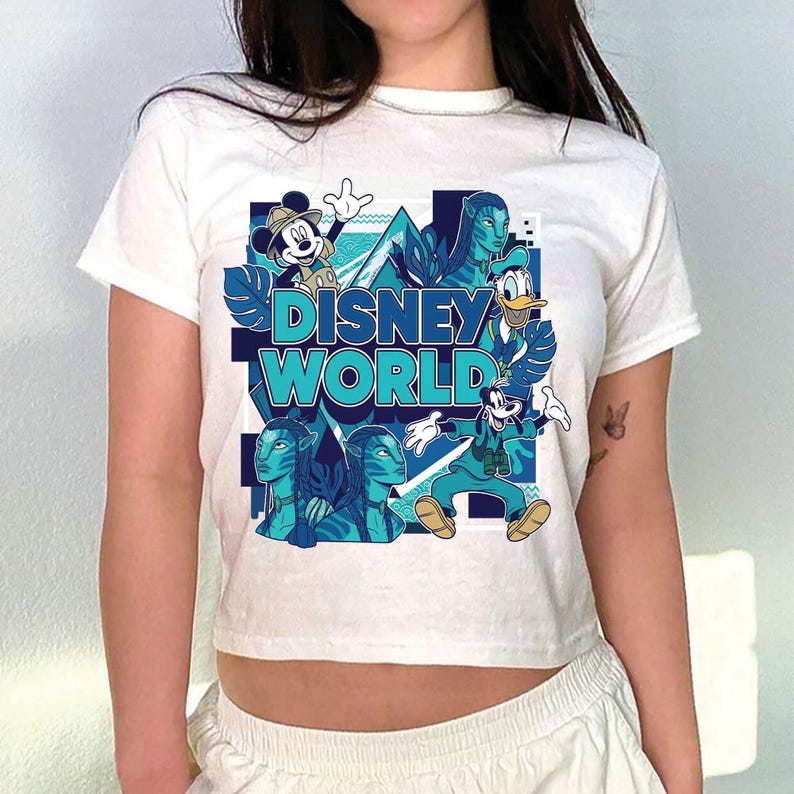 Puede incluir: Camiseta blanca con un dise&ntilde;o de Disney World. El dise&ntilde;o incluye a Mickey Mouse, el Pato Donald, Goofy y personajes de Avatar, en tonos azules y turquesas. Las palabras "DISNEY WORLD" se muestran de forma destacada.