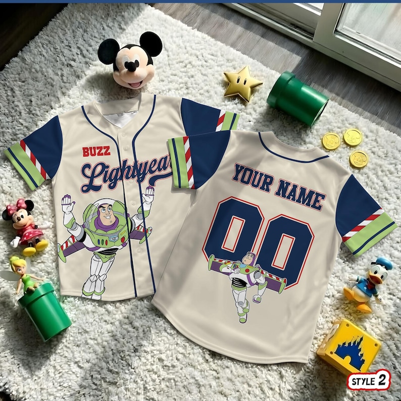 May include: Two beige baseball jerseys with navy blue sleeves and Buzz Lightyear graphics. One jersey says "Buzz Lightyear" and the other says "Your Name" with the number "00". The jerseys are surrounded by Disney-themed toys.