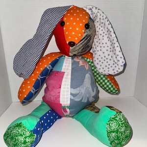 May include: A handmade patchwork bunny rabbit doll with mismatched fabrics in various colors and patterns. The bunny features orange polka dots, blue gingham, and floral prints. The doll has long floppy ears and is sitting upright.