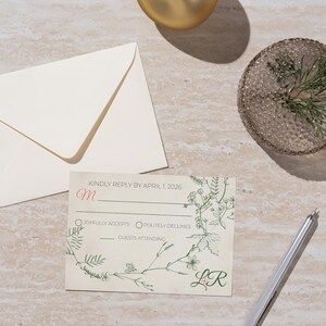 May include: A wedding response card with floral design and the text "KINDLY REPLY BY APRIL 1, 2026". The card includes options to accept or decline, with space for guest count. A matching envelope and pen are also present.
