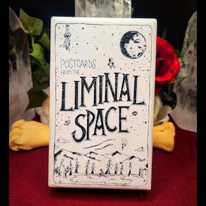May include: A rectangular white deck of cards featuring black line art illustrations of a rocket, an astronaut, a moon, and a landscape with trees and mountains. The text reads Postcards From The Liminal Space in a stylised black font.
