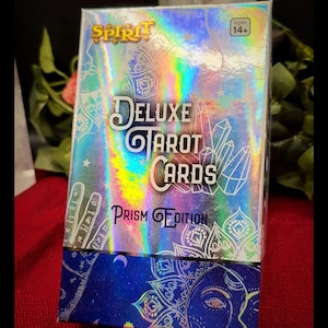 Op de afbeelding: Deluxe Tarot Cards Prism Edition doos met een holografische iriserende afwerking. De doos heeft het woord "Spirit" in goud en de woorden "Deluxe Tarot Cards" in wit. De onderkant van de doos is blauw met een zon- en maanontwerp.