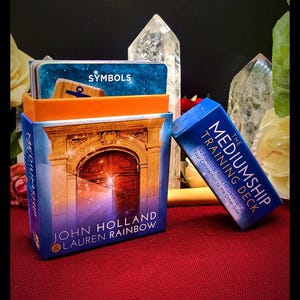 May include: A blue and orange box set titled The Mediumship Training Deck by John Holland and Lauren Rainbow. The box features an illustration of a stone archway with a wooden door and contains a deck of cards with the word Symbols printed on top.