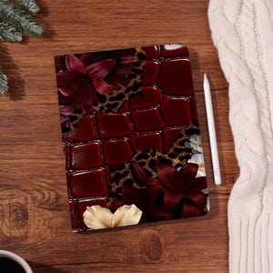 May include: A rectangular tablet case featuring a deep burgundy faux-alligator skin texture, a black and gold leopard print pattern, and large dark red and cream-colored lily flowers. A white stylus is positioned next to the tablet case.