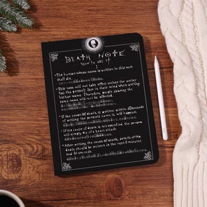 Può includere: Una tazza di ceramica bianca con un manico nero e la scritta "But First, Coffee" in nero, con un carattere a mano. La tazza è su una superficie bianca.