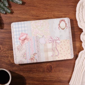 Könnte beinhalten: Eine Laptop-Hülle mit einem Patchwork-Design aus sanften Pastellmustern, darunter hellblaues Vichy-Karo, Blumenmuster, ein rosa Umschlag mit Schleife, ein kleiner Hase, ein dekorativer ovaler Rahmen und eine große rosa Schleife.