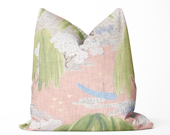 May include: A decorative pillow with a landscape design. The pillow features a pink background with a scene of trees, a boat, and birds. The trees are green and white, and the boat is blue. The pillow is a square shape.