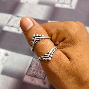 May include: Two silver rings worn on a thumb, each featuring a V-shaped design with a row of small, raised metal spheres along the outer edge. The rings have an oxidised finish that highlights the textured, beaded detailing on the metal bands.