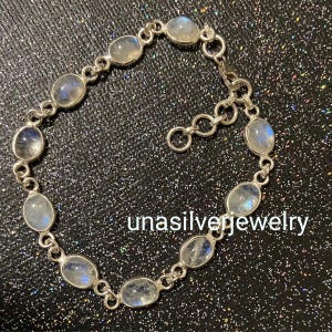 May include: A silver bracelet featuring oval-shaped moonstone gemstones. The bracelet is composed of interconnected links, with each link holding a moonstone. The text "unasilverjewelry" is visible on the image.